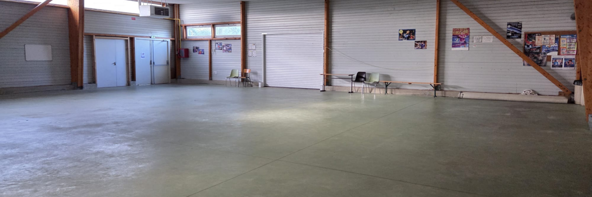 Salle vide avec sol en béton, tables, chaises, portes et affiches murales.
