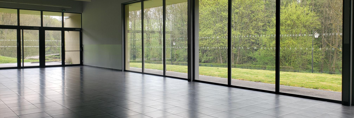 Salle vide avec grandes baies vitrées.