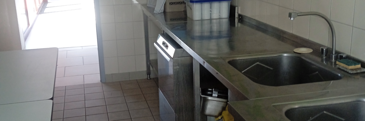 Cuisine avec plans de travail, double évier, lave-linge, frigo, et armoires.