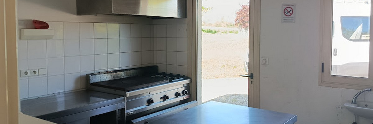 Cuisine avec plaques de cuisson, hotte, évier, table de travail et porte ouverte.