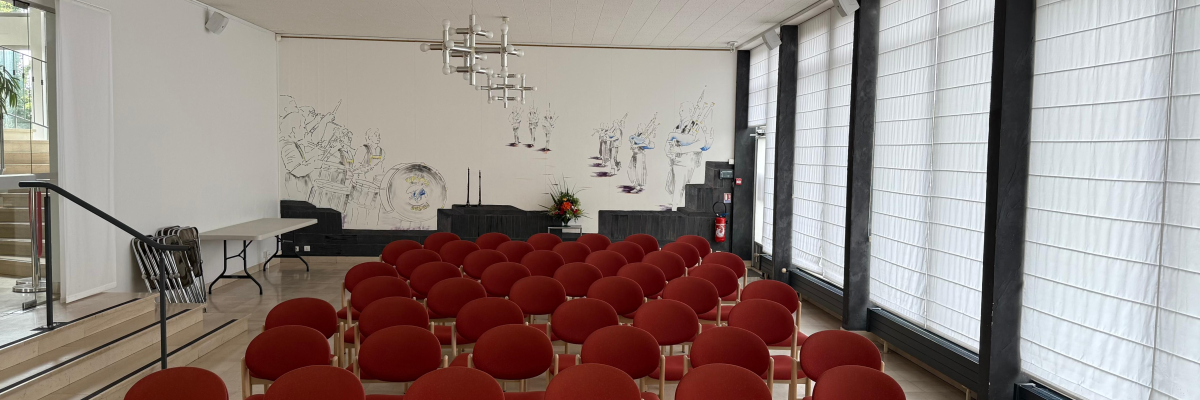 "Salle avec chaises, tableau blanc, rideaux, projecteur, système audio et éclairage."