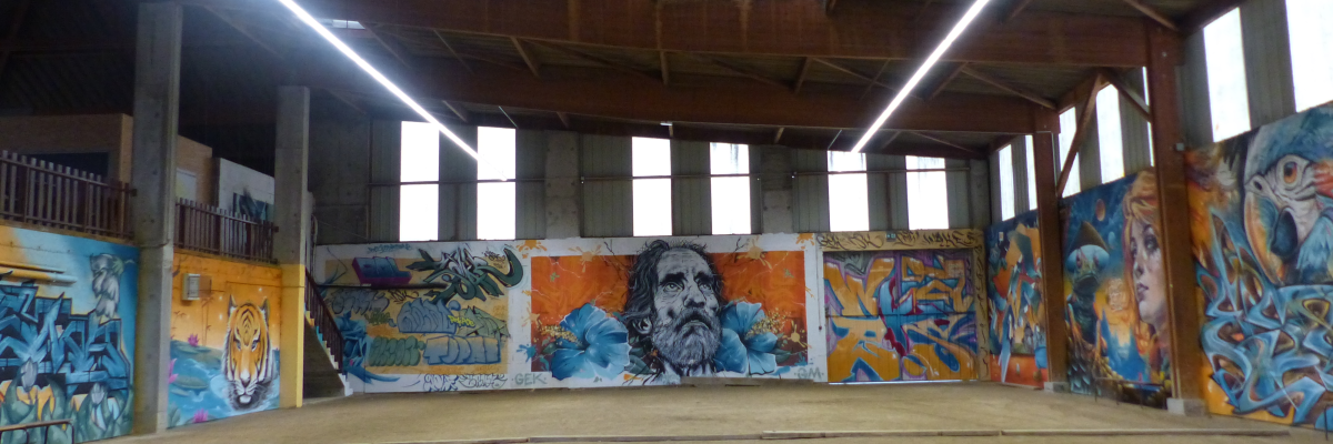 Atelier avec graffitis muraux, sol en béton, fenêtres et éclairage fluorescent.