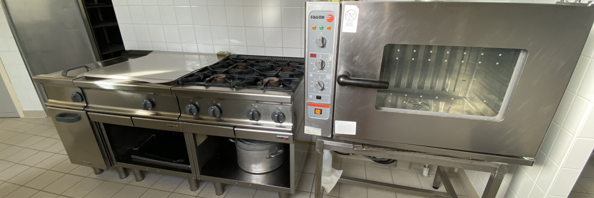 Cuisine avec four industriel, plaque de cuisson, hotte aspirante et plan de travail.