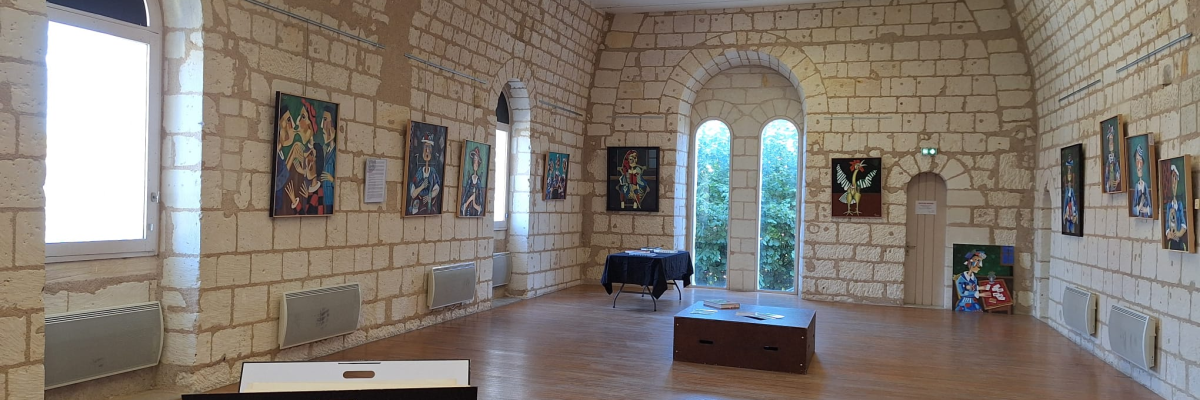 Salle avec murs en pierre, tableaux, fenêtres, tables, et radiateurs.