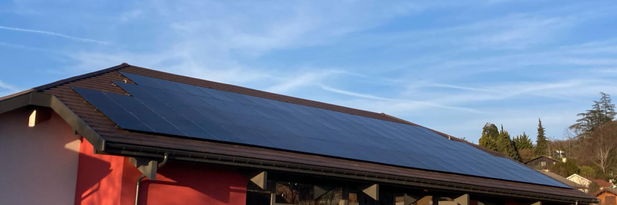 Bâtiment avec panneaux solaires sur le toit, murs rouges, grandes portes et fenêtres.