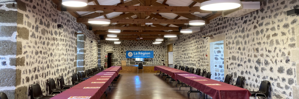 Salle de réunion avec tables, chaises, et écran d'affichage.