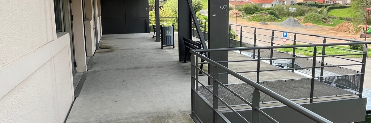 Couloir extérieur avec rambarde et vue sur terrain.
