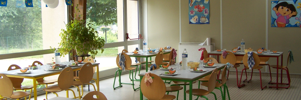 Salle de classe avec tables, chaises, nappes, ballons, nourriture, plantes, et décorations murales.