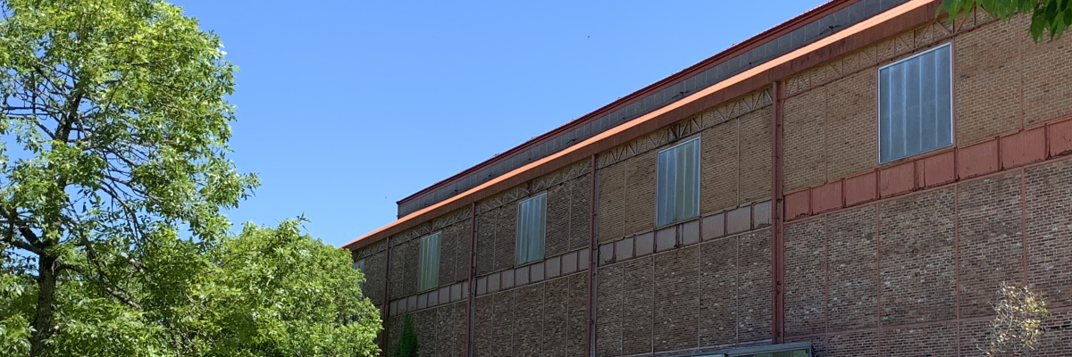 Bâtiment en brique avec fenêtres, pelouse, arbres et ciel bleu.
