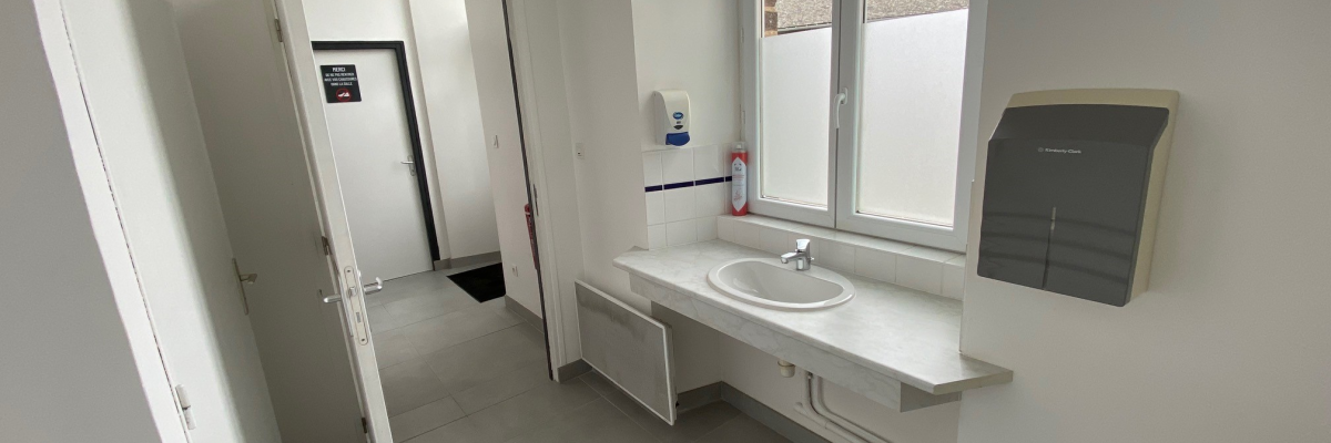 Salle de bain avec lavabo, miroir, radiateur, sèche-serviettes et tabouret.