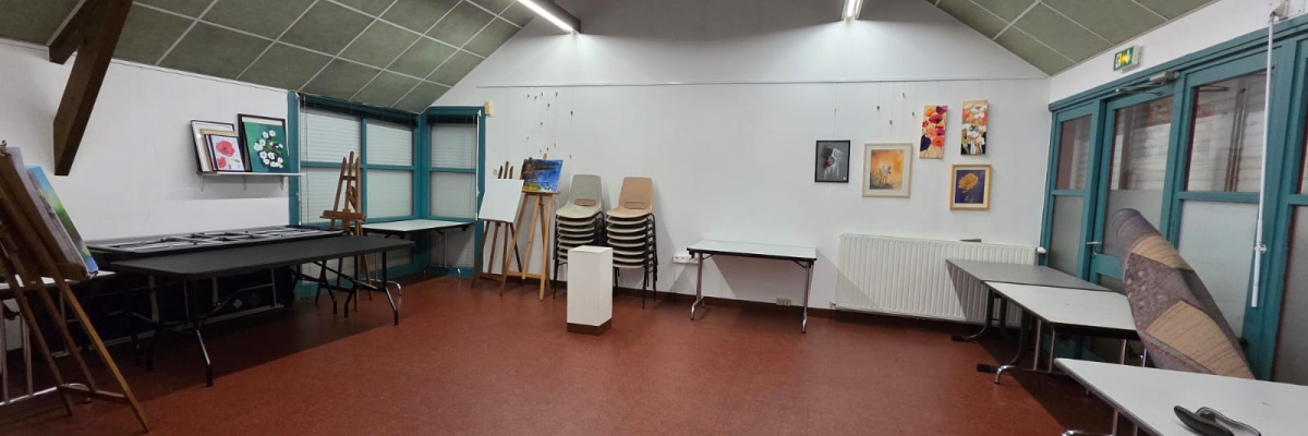 Salle avec tables, chaises, radiateur, tablettes, tableaux, porte-manteaux, échelles et lumières.