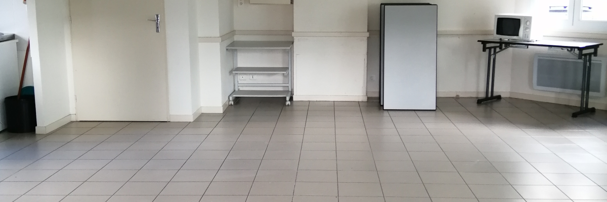 Pièce vide avec sol carrelé, frigo, table, évier et porte.