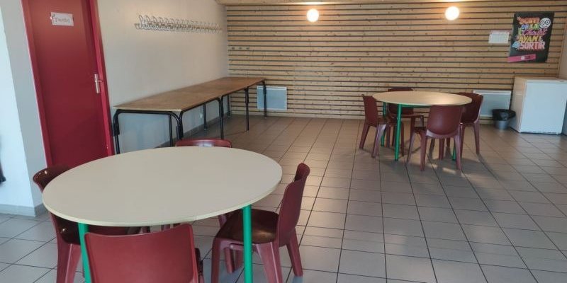 Salle avec tables, chaises, horloges, porte rouge et radiateur.