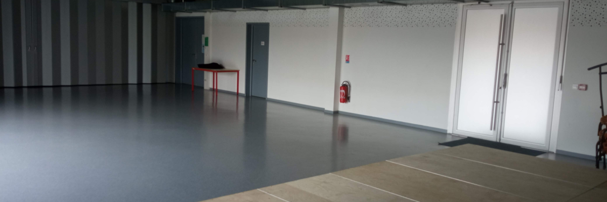 Grande salle vide avec porte, table rouge, extincteur et porte-manteau.