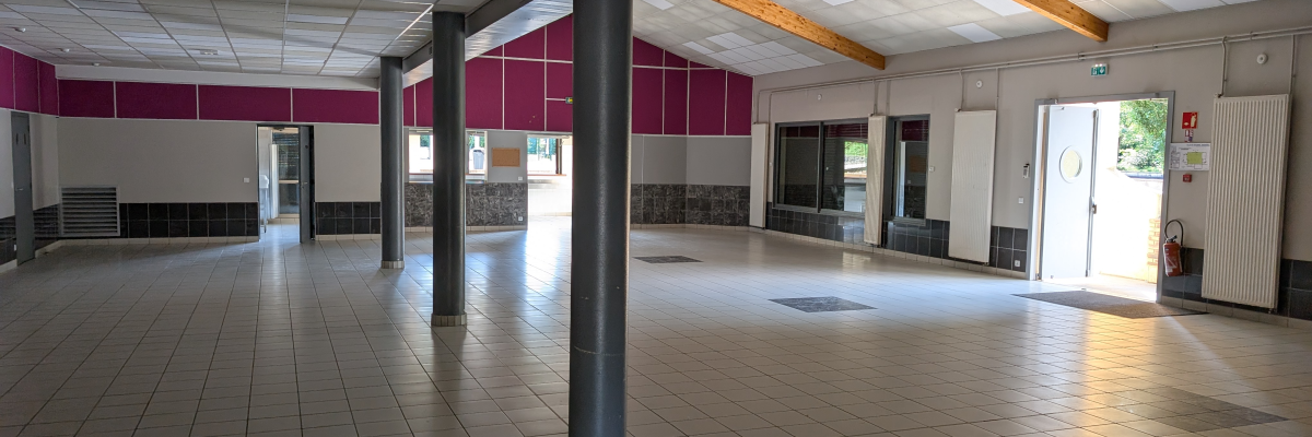 Grand espace vide avec colonnes, portes, fenêtres et sorties de secours. Sol carrelé, murs rose et plafond avec dalles.