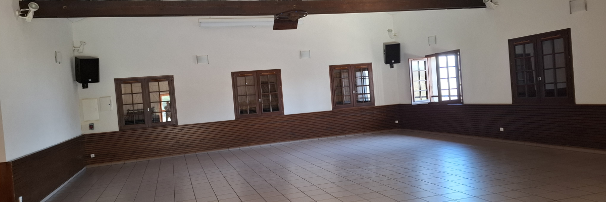 Salle vide avec poutre apparente, portes, fenêtres et haut-parleurs muraux.