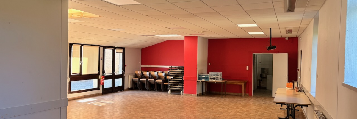 Salle avec tables, chaises, tableau blanc, équipement audio et éclairage au plafond.