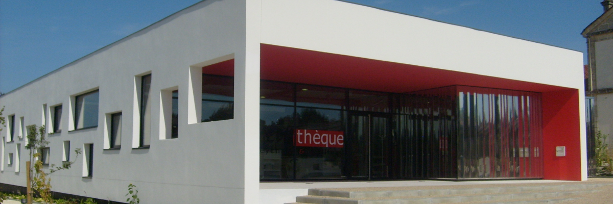 Bâtiment moderne avec façade blanche, grandes baies vitrées, entrée rouge, escalier et gravier.