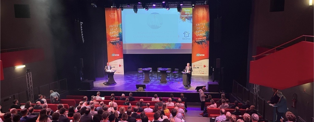 Salle de conférence avec écran, projecteur, podium, tables, chaises et public.