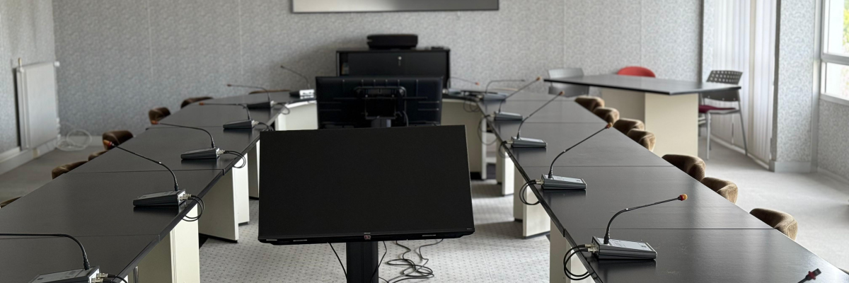 Salle de réunion avec tables, chaises, écrans, vidéoprojecteur et ordinateurs.