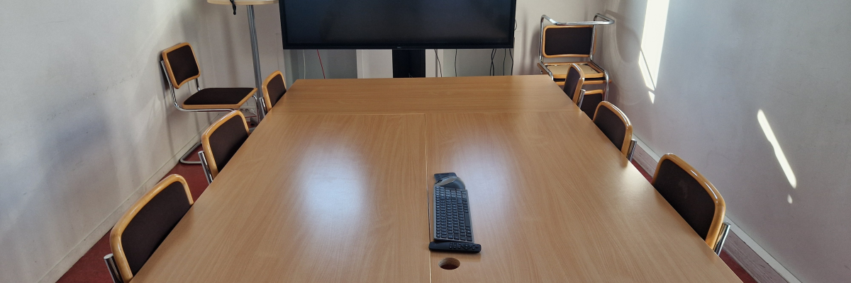 Salle de réunion avec table, chaises et écran.