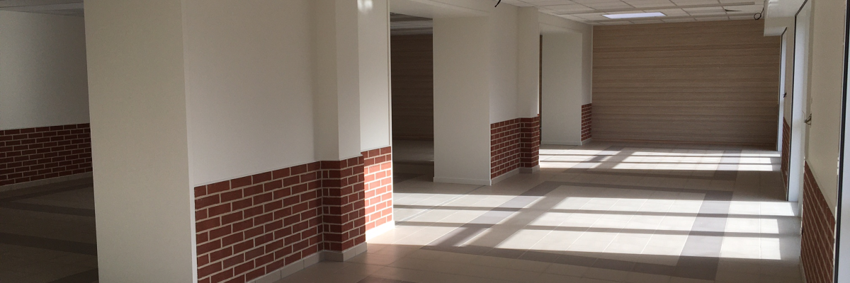 Couloir avec murs blancs, bande de briques, sol carrelé. Porte, lumières au plafond.