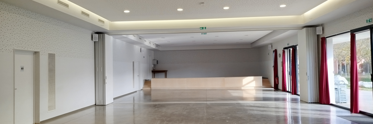 Salle spacieuse avec plafond à spots, sol poli, portes vitrées, murs blancs.