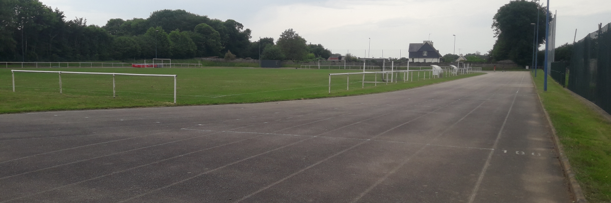 Terrain de sport avec piste d'athlétisme, pelouse et but de football.