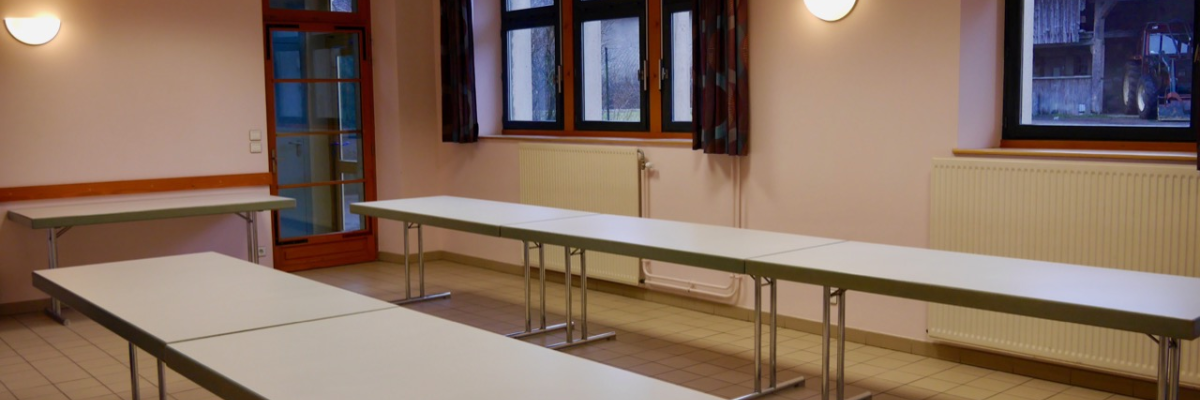 Salle avec tables, chaises, fenêtres et éclairage mural.