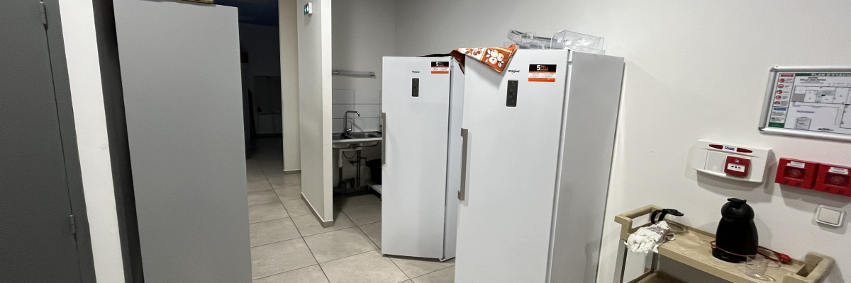 Pièce avec réfrigérateurs, étagères, chariot, armoire et écran mural.