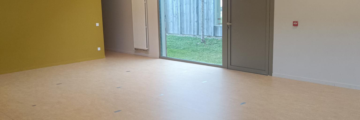 Salle vide avec porte, fenêtre, sol en bois et murs colorés.