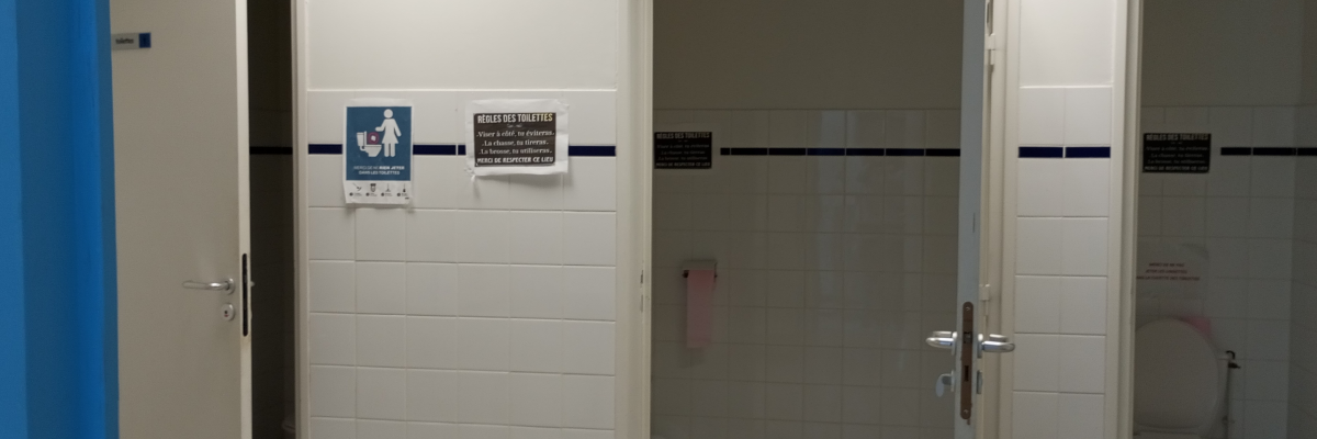 Toilettes avec portes ouvertes, urinoirs, toilettes, lavabo et panneaux indicateurs.