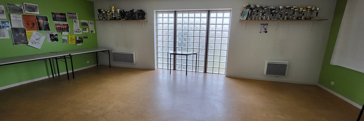 Salle spacieuse avec murs verts, tableaux d'affichage, étagères, portes vitrées, et radiateurs.