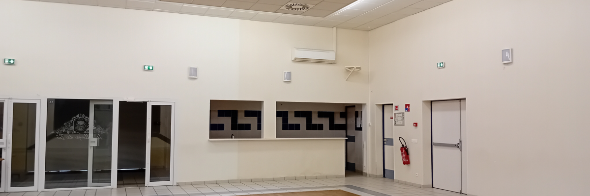 Salle vide avec portes, climatiseur, extincteur et sorties de secours.