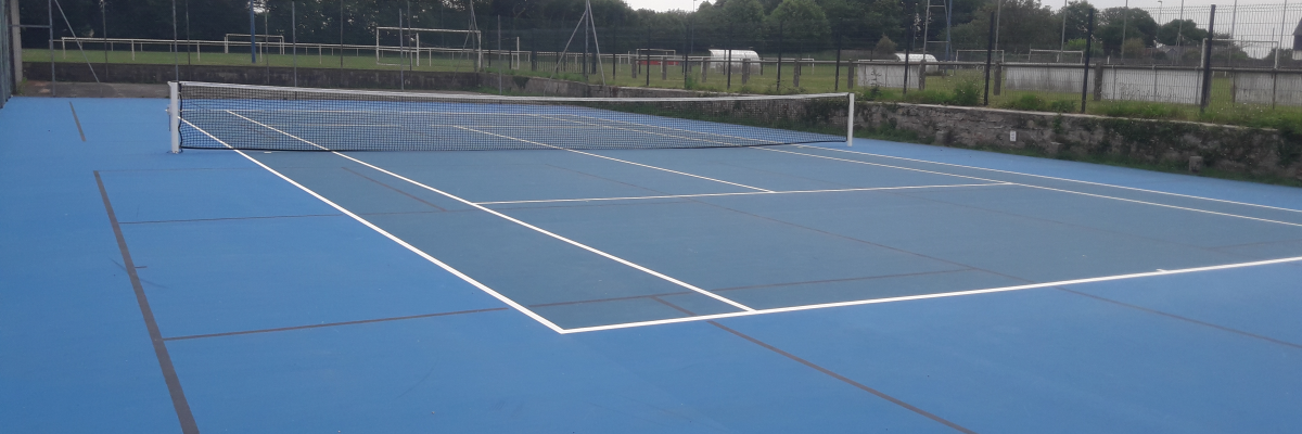 Terrain de tennis bleu avec filet, clôture et arbres en arrière-plan.