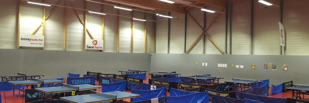 Salle de sport avec tables de ping-pong, filets et raquettes.