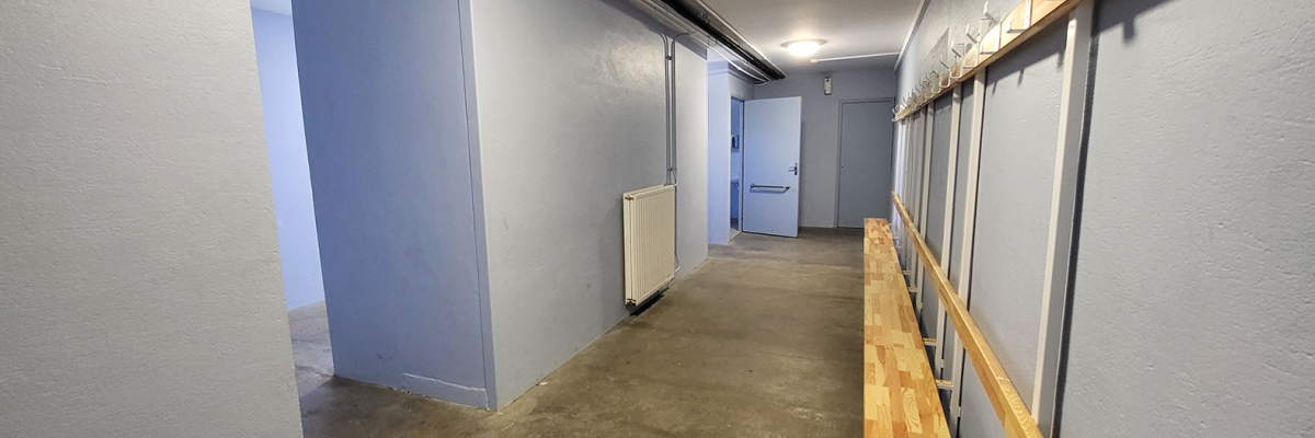 Couloir avec porte, radiateur, banc en bois et patères murales.