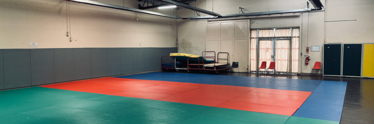 Salle avec tapis colorés, trampoline, chaises et armoires.