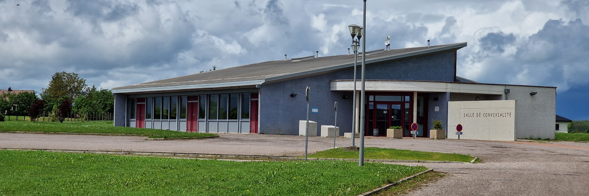 Bâtiment avec toiture plate, devantée par un lampadaire, une pelouse et une allée.