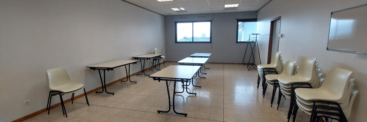 Salle avec tables, chaises, tableau blanc et fenêtre.