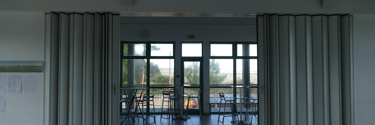 Salle avec porte vitrée, tables, chaises, extérieur visible.