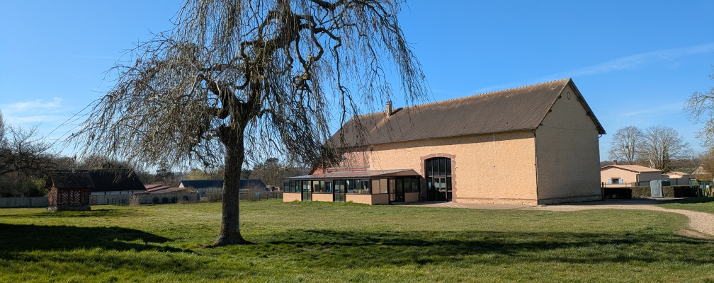 Bâtiment avec grand arbre devant, pelouse, ciel dégagé.