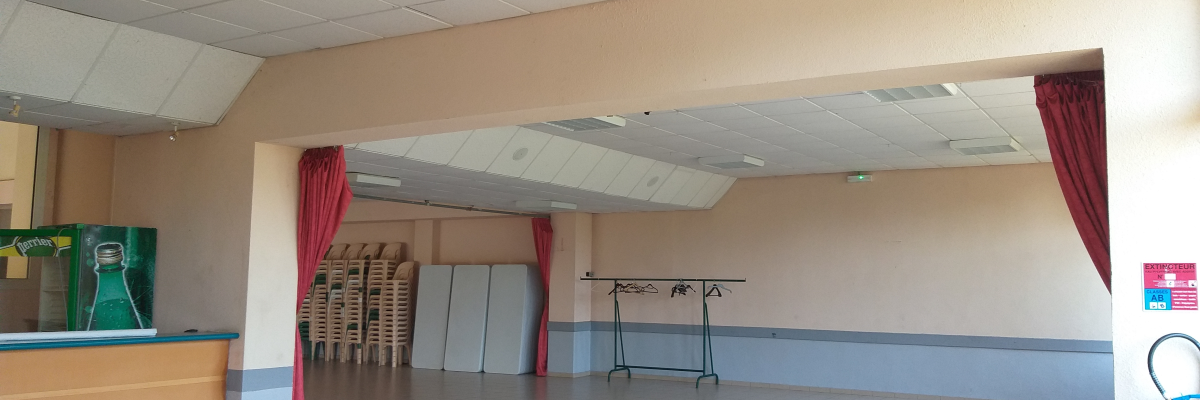 Salle vide avec rideaux, porteurs de vêtements, chaises empilées et extincteur.