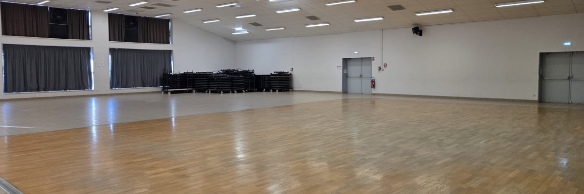 Salle avec parquet, éclairages au plafond, gradins, portes et extincteur.