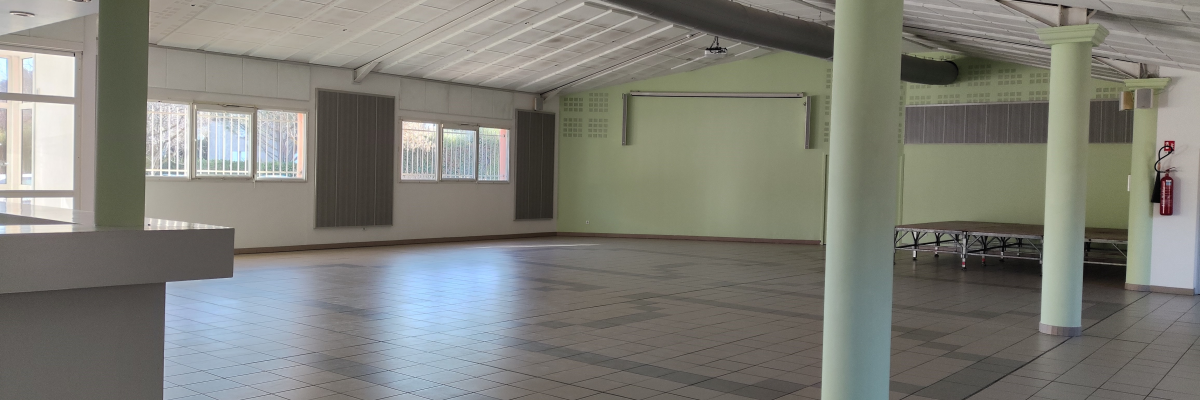 Espace vide avec colonnes, tables, chaises, fenêtres, extincteur et poubelle.