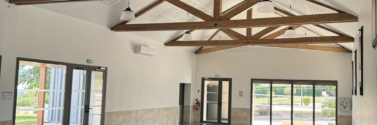 Salle avec piliers, tables, chaises, et grandes fenêtres.