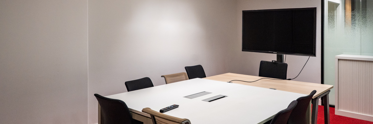 Salle de réunion avec table, chaises, écran, télécommande.