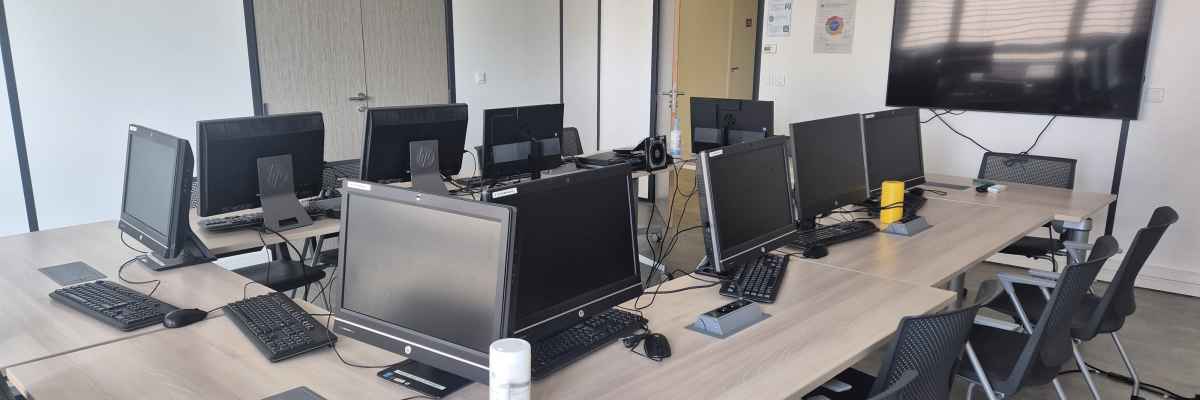 Salle avec table, chaises, écran, ordinateurs et claviers.