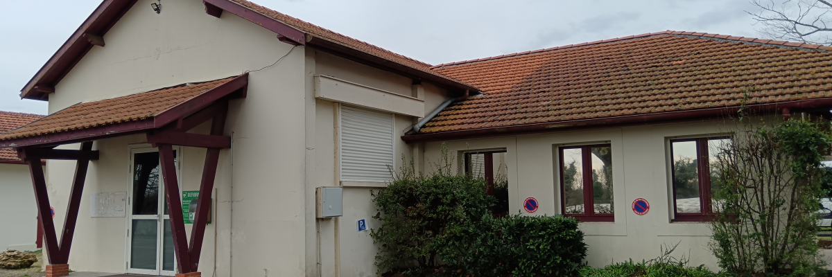 Bâtiment avec toit en tuiles, murs blancs, fenêtres et porte en verre. Arbres sans feuilles à proximité.