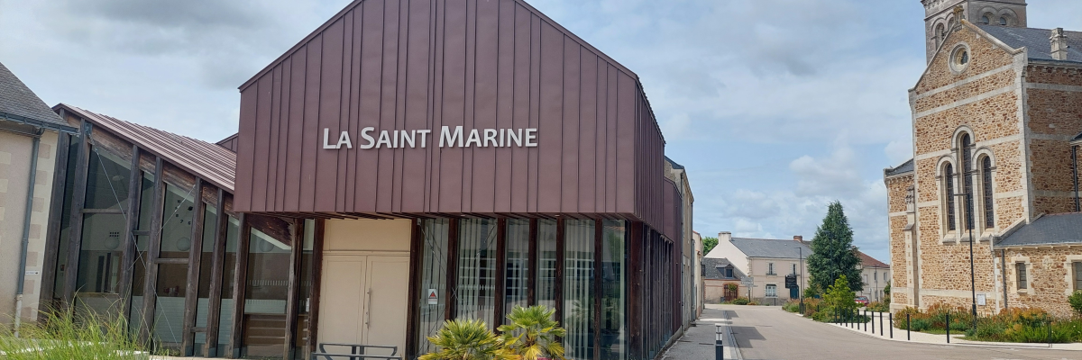 "Bâtiment moderne avec enseigne, devant une église et une route."